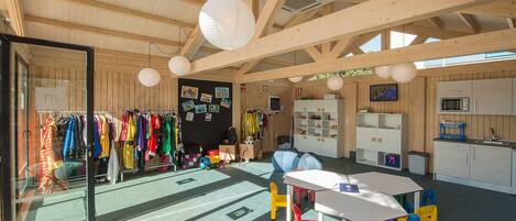 A spacious room with a high ceiling, wooden beams, a dining area with colorful chairs, a kitchen with a microwave, and a rack of colorful clothes.