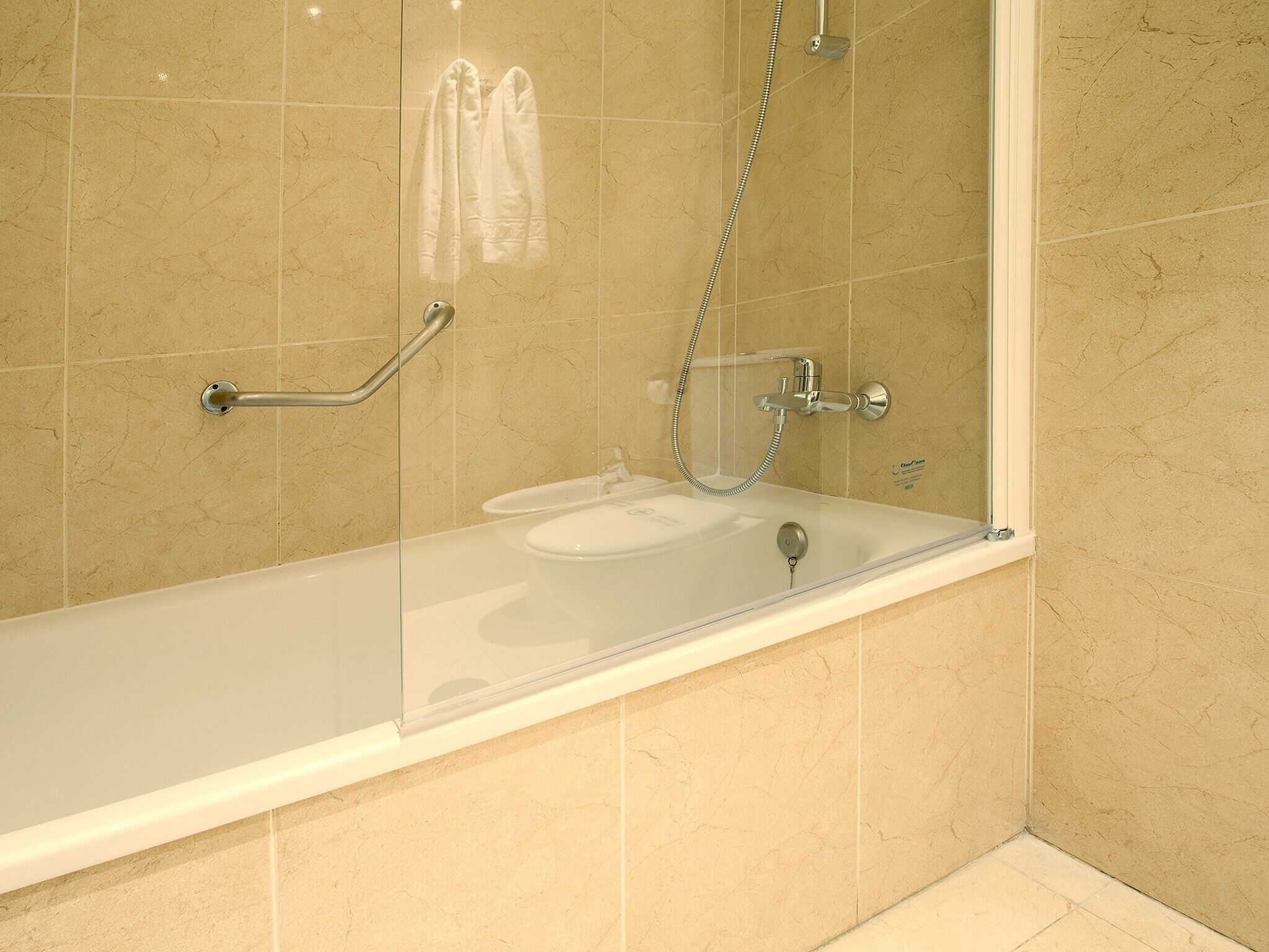 Ein modernes Badezimmer mit einer Glaskabine um das Bad, einer Duschbrause und einer Haltestange.