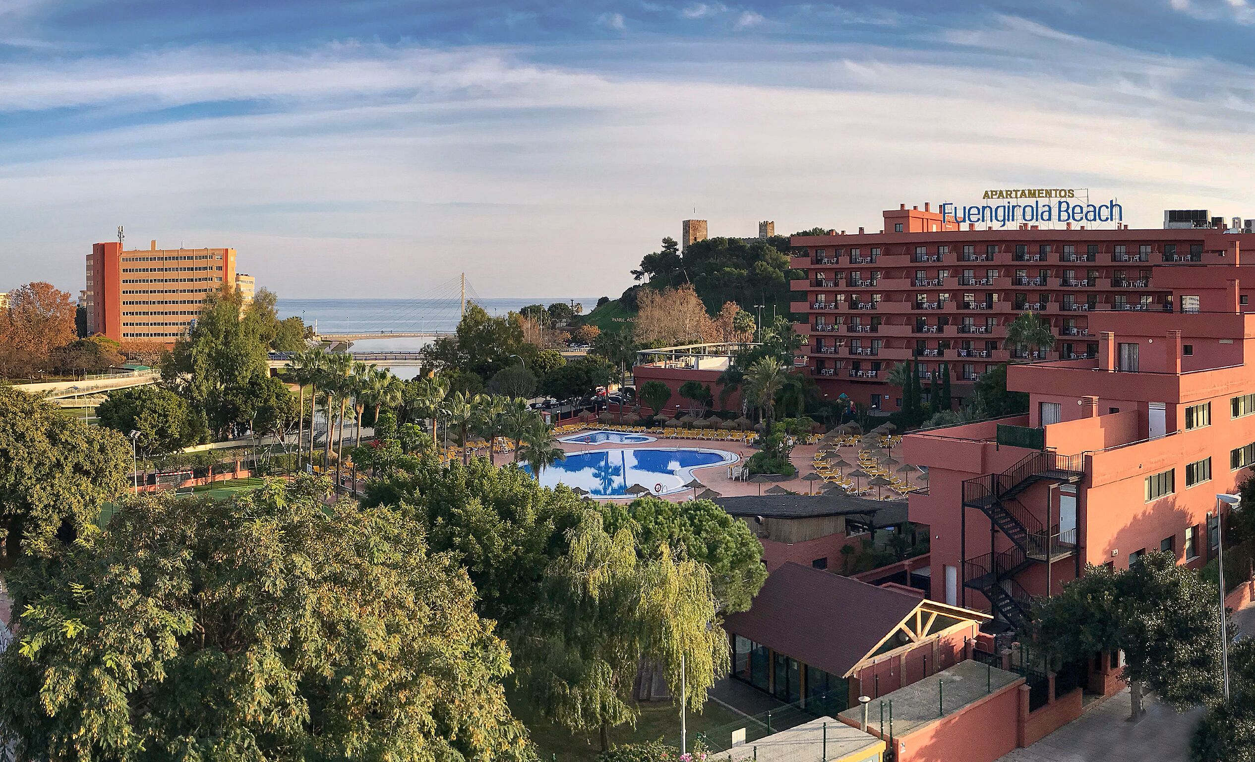 A hotel with a pool, surrounded by trees and a view of the ocean.