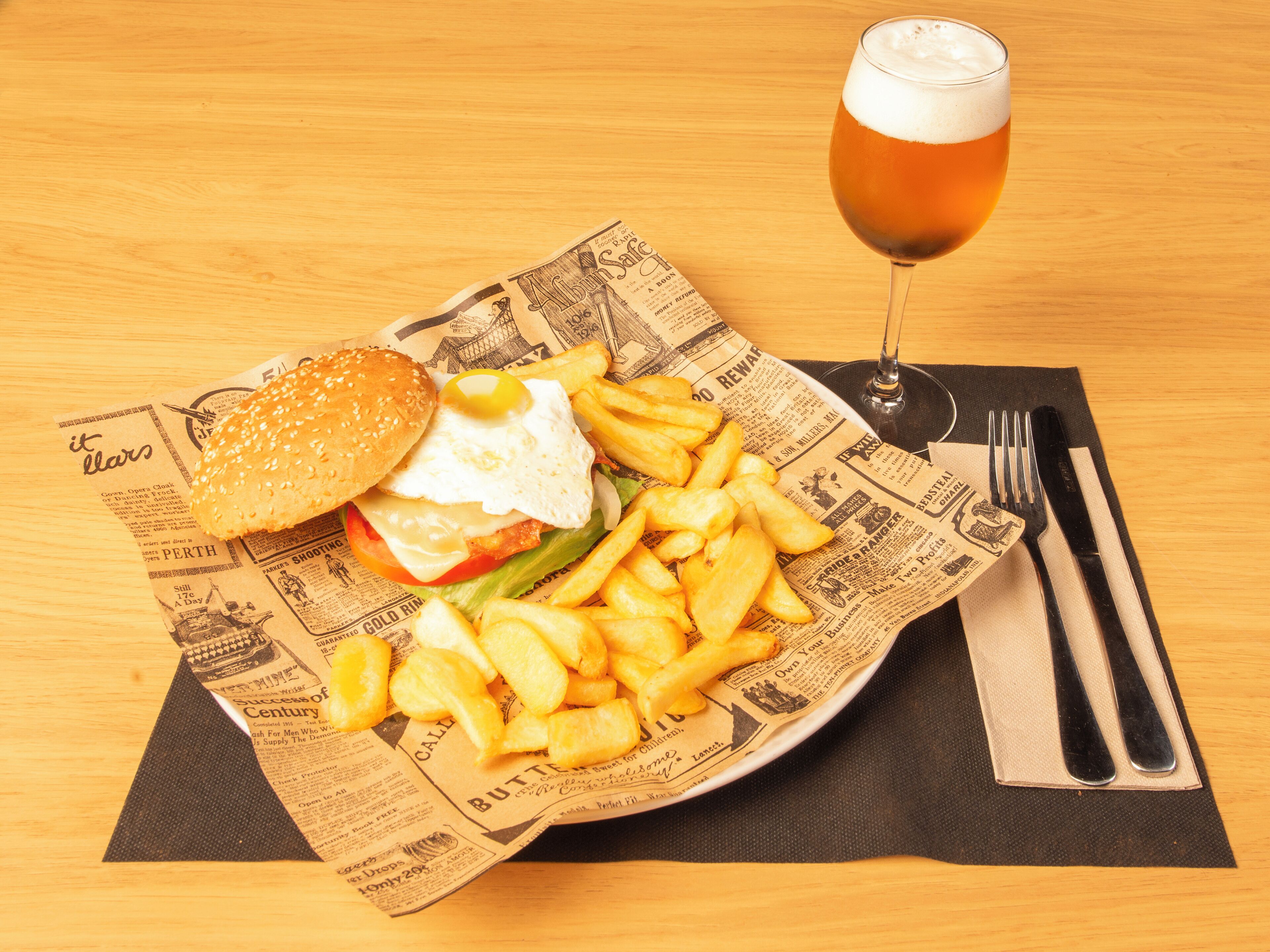 A meal consisting of a burger, fries, and a glass of beer on a wooden table.
