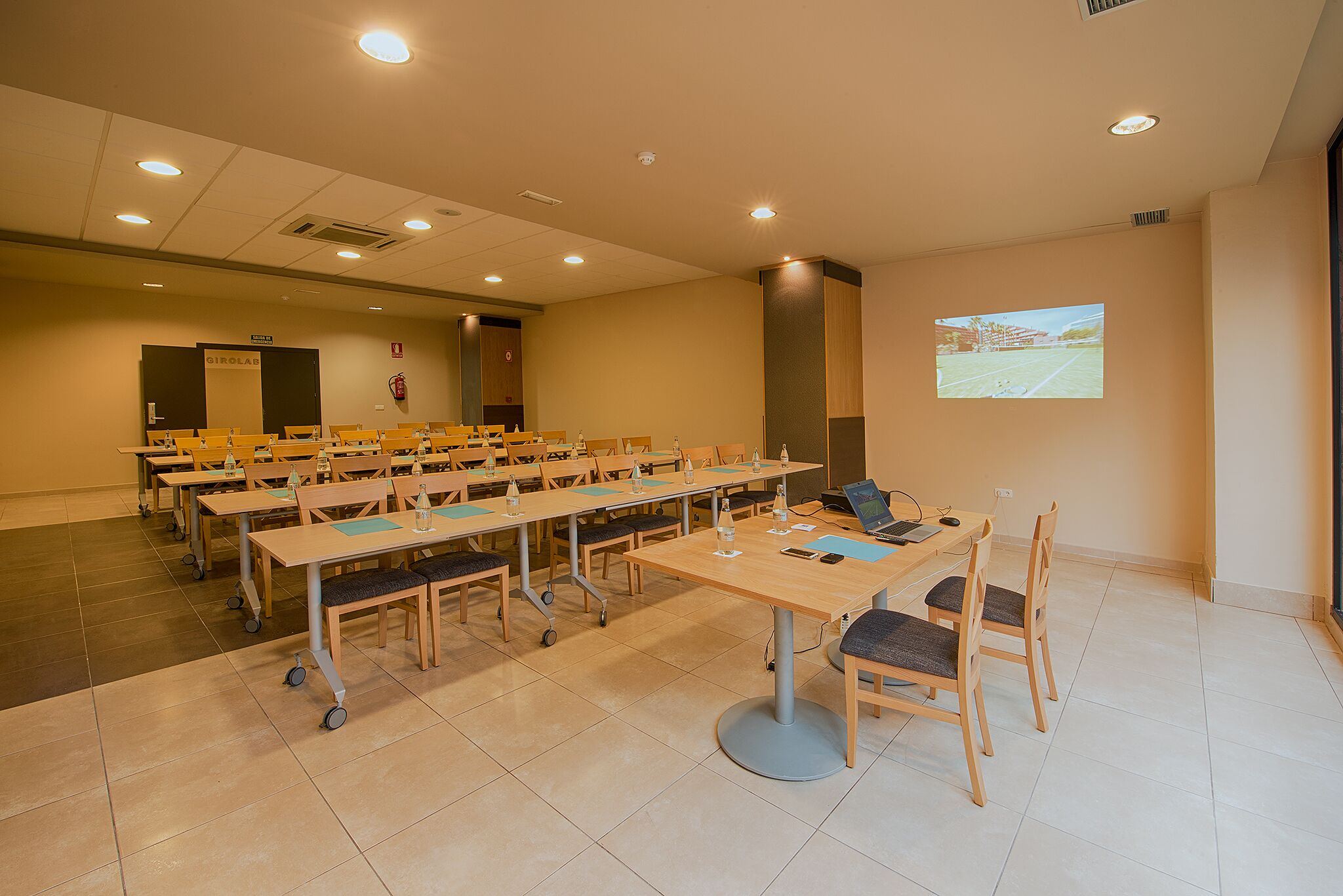 Une salle de conférence dotée de plusieurs tables et chaises, ainsi que d’ordinateurs portables et de bouteilles d’eau.