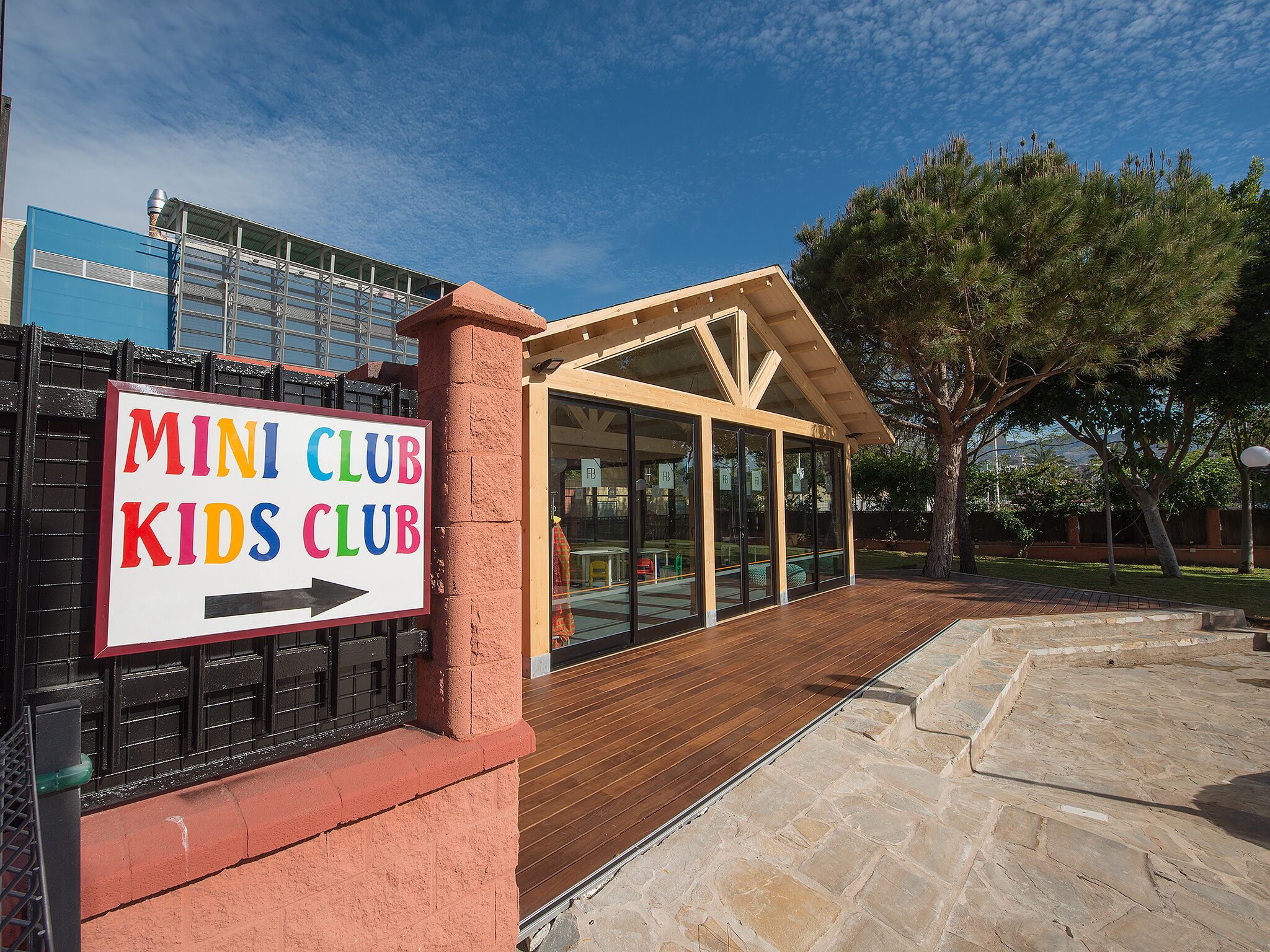 Un edificio con un cartel que dice "MINI CLUB KIDS CLUB" y una zona de cubierta de madera.