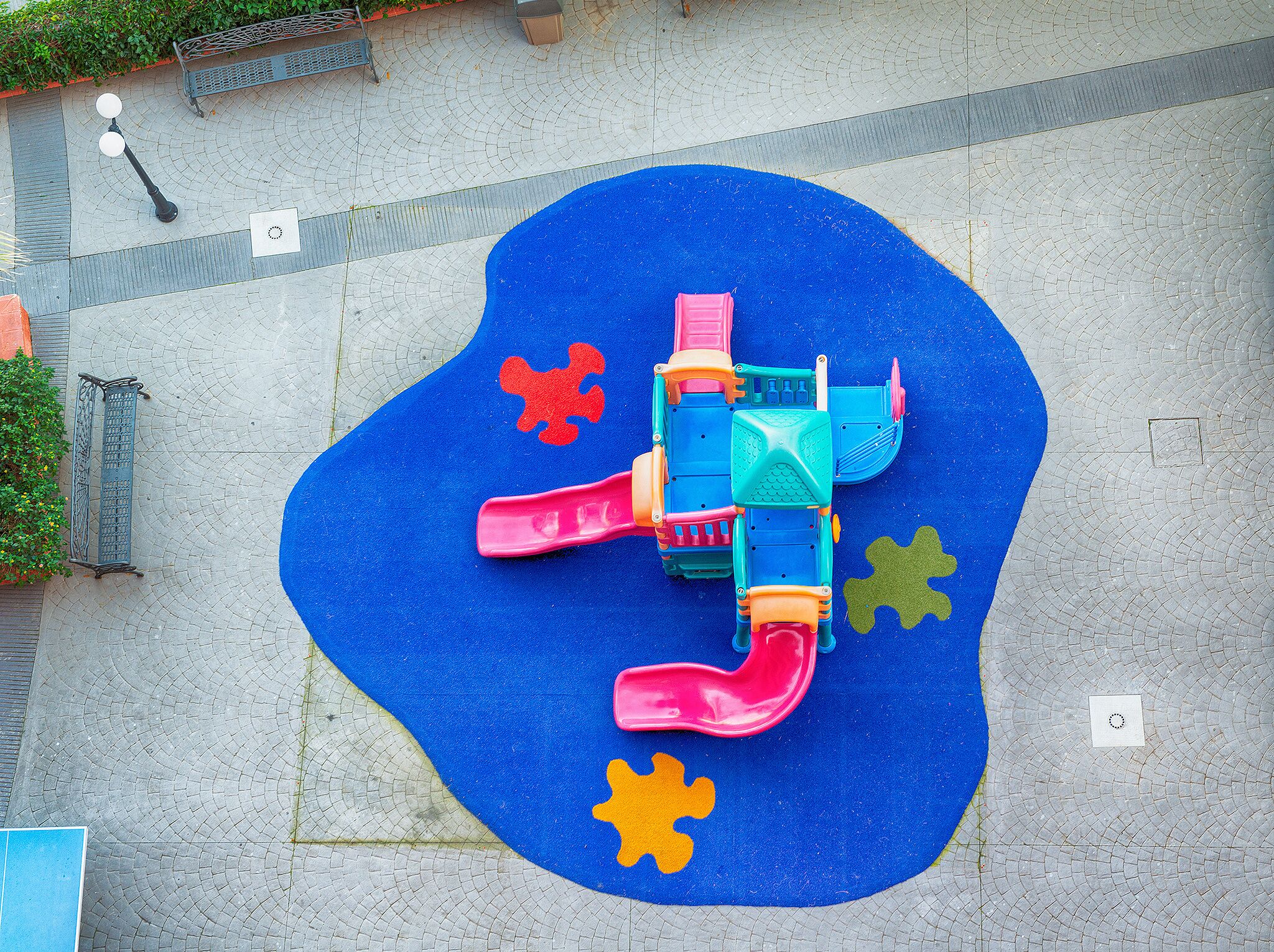 Un parque infantil con suelo de goma azul, un tobogán y piezas de rompecabezas de colores.