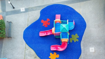 Un parque infantil con suelo de goma azul, un tobogán y piezas de rompecabezas de colores.