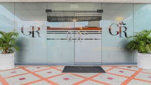 A building entrance with glass doors displaying the letters "GR" and a logo. There are potted plants on either side of the entrance. - TAMA Hotel Granada Real Cali (Cali)
