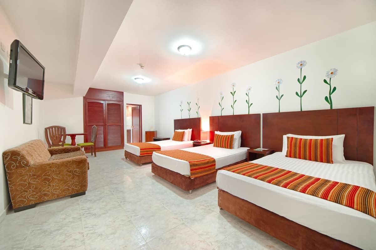 Habitación de hotel con sofá, dos camas individuales, una cama doble, televisor y pared decorada con pinturas de flores.