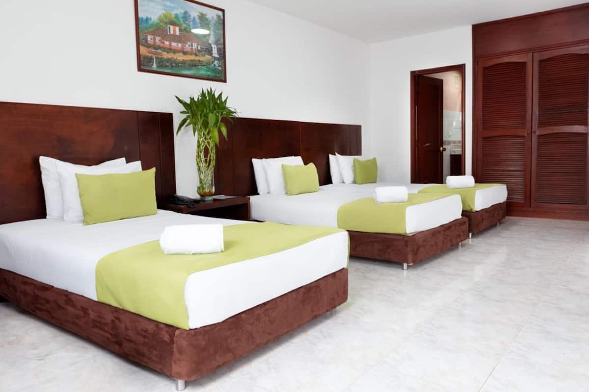 Una habitación de hotel con tres camas, cada una con ropa de cama blanca y verde, un cabecero de madera y una planta en maceta.