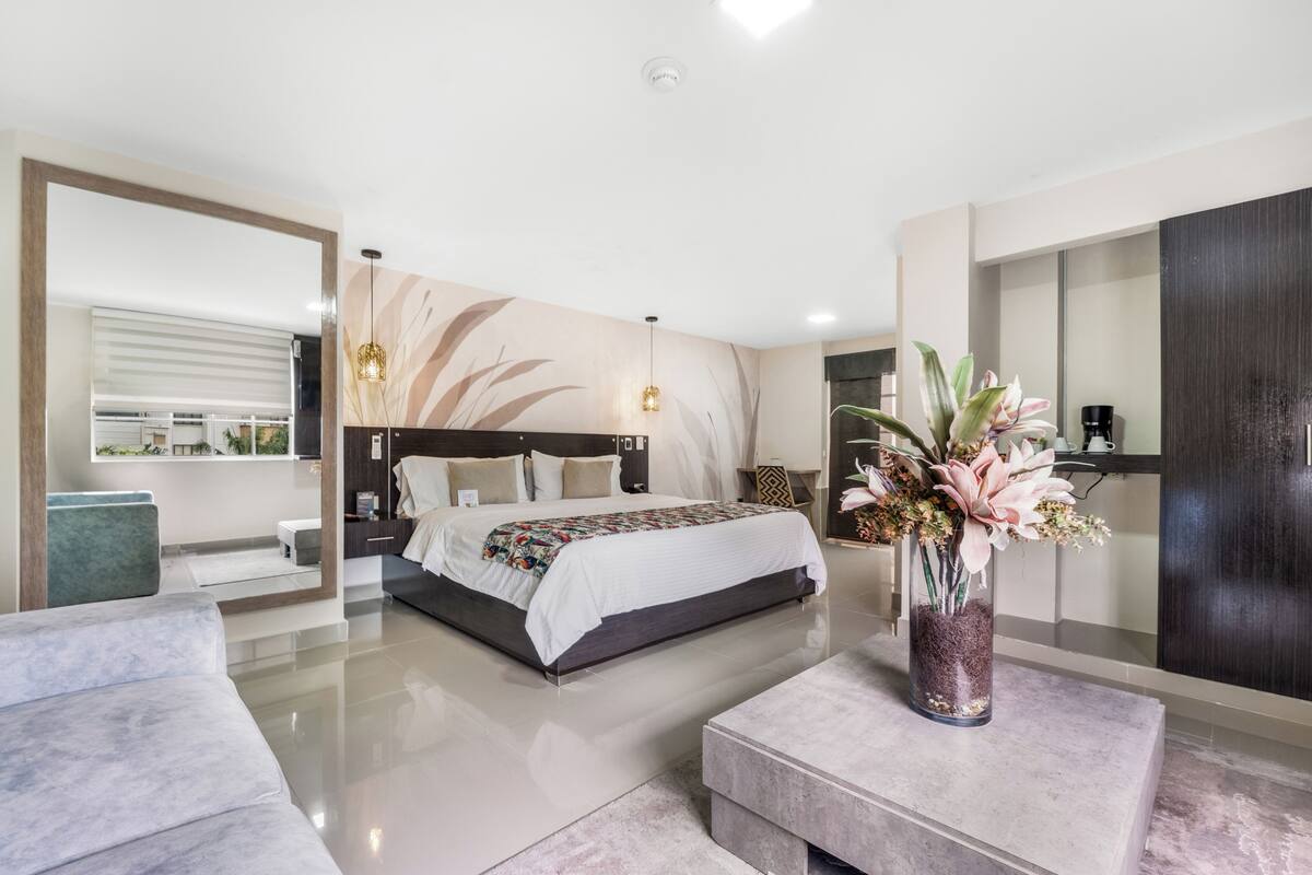 Quarto moderno com uma cama grande, uma mesa de cabeceira, uma luminária e um vaso de planta, com vista para o exterior.