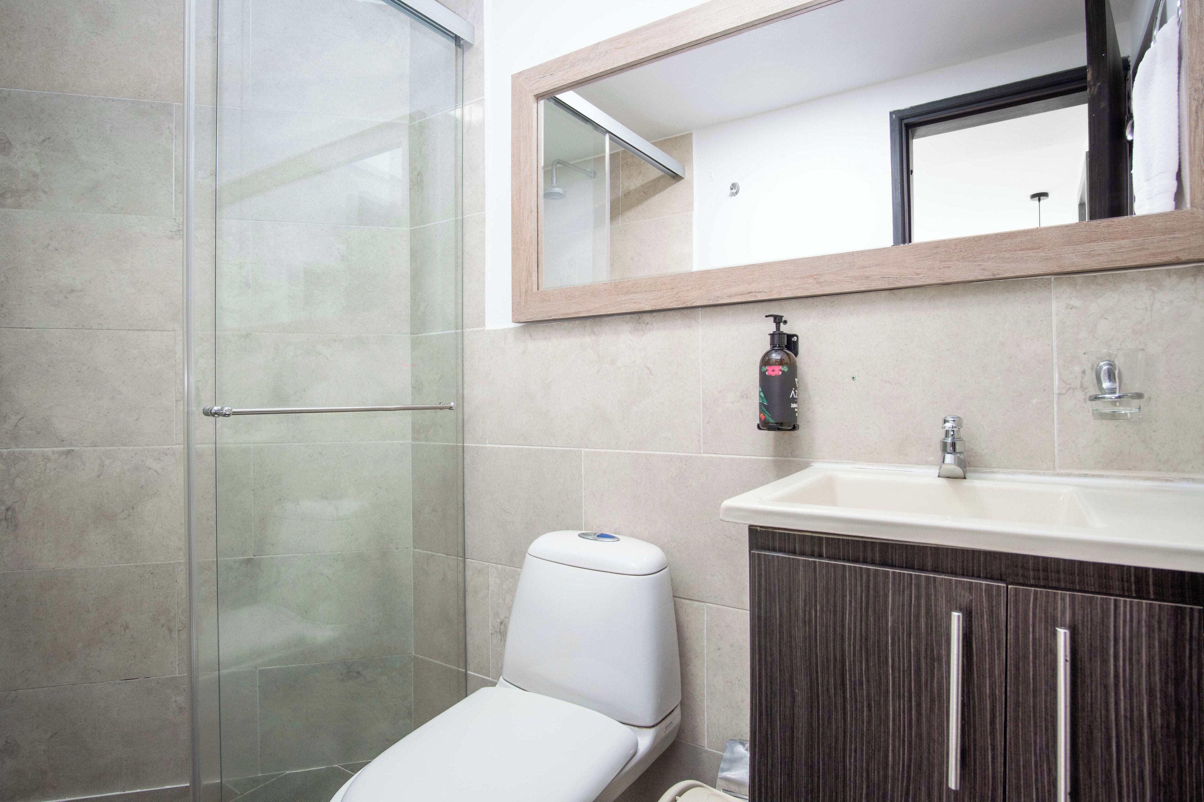 A modern bathroom with a glass shower enclosure, a toilet, a sink with a mirror above it, and a cabinet below.