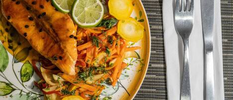 A plate of food with salmon, carrots, and potatoes, accompanied by a fork and knife on a table.