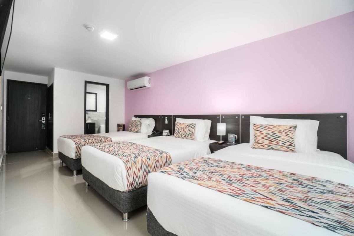 Quarto de hotel com três camas, um espelho, um aparelho de ar condicionado e uma porta.