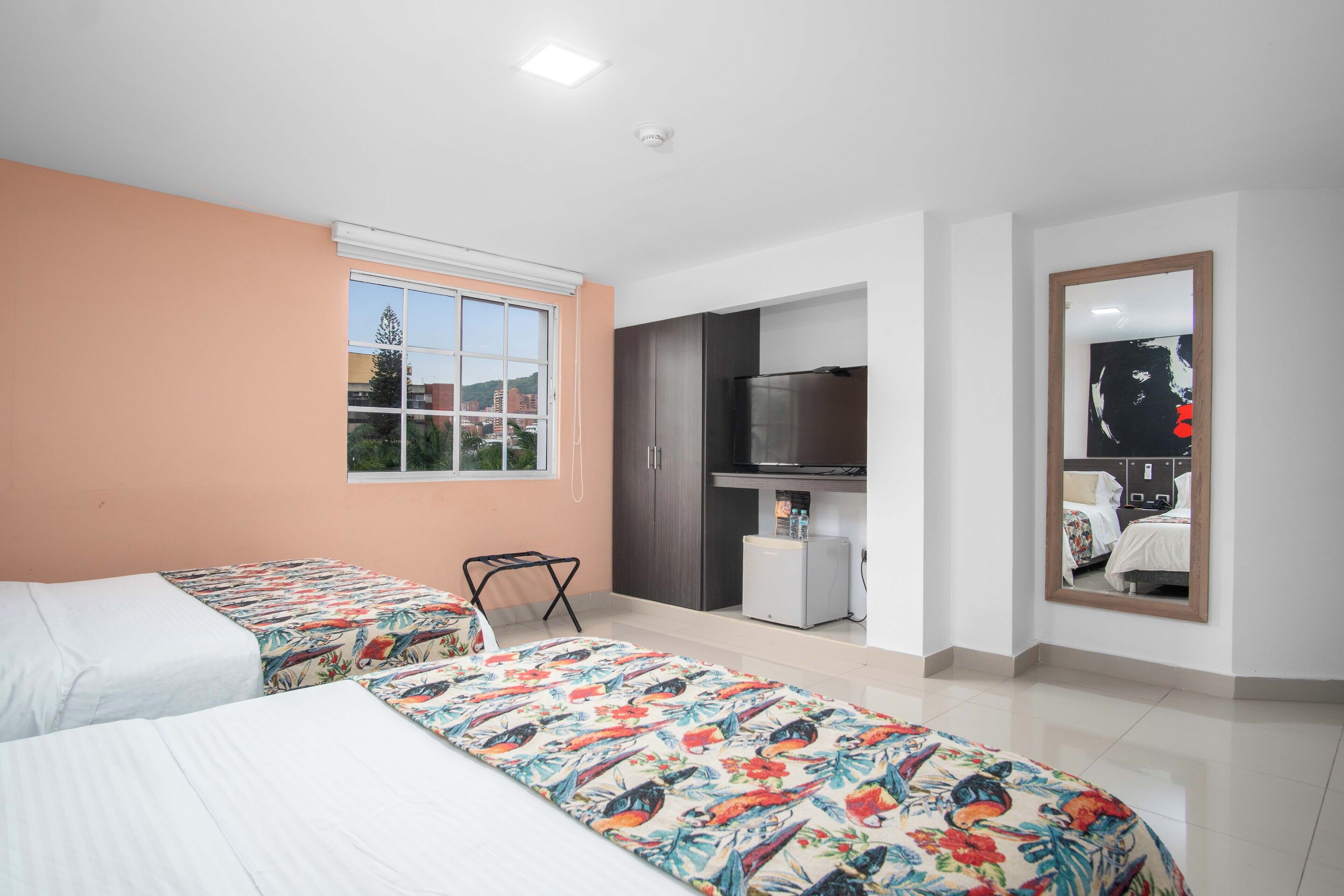 Una habitación de hotel con dos camas, una kitchenette pequeña, un televisor y un espejo.