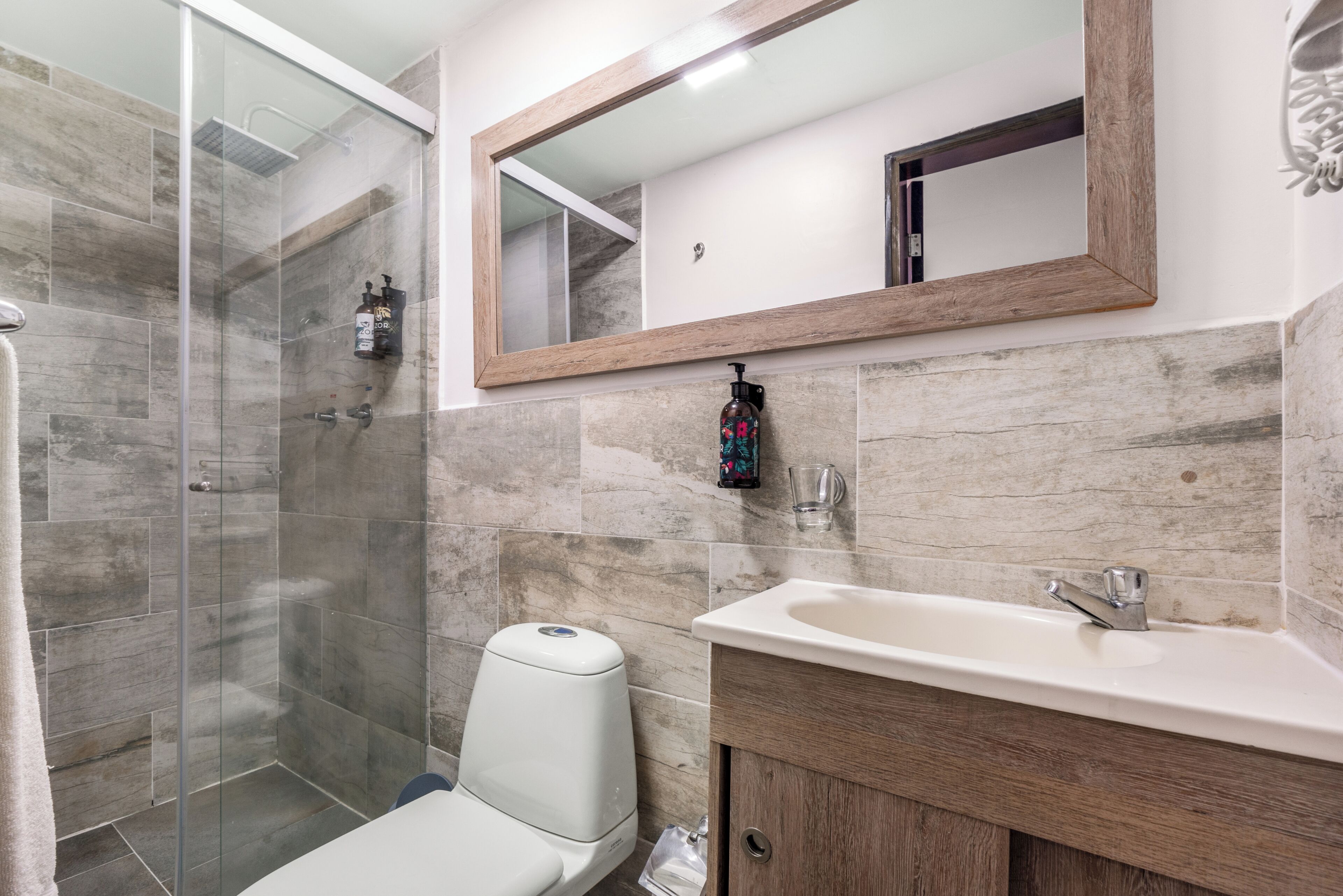 A bathroom with a glass-enclosed shower, a white toilet, a sink with a wooden cabinet, and a mirror above the sink.