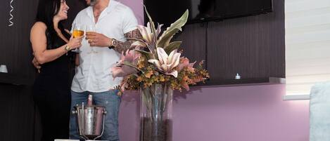 A couple holding drinks, a large illuminated 'TEAMO' sign, and a vase with flowers.