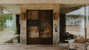 A rustic wooden door with a plaque, a stone bench, and a glass wall reflecting a landscape.