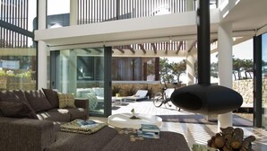 A modern living room with a large sectional sofa, a coffee table, and a fireplace. There is a balcony with a railing and a view of the outdoors. - Areias do Seixo Charm Hotel & Residences (Torres Vedras)