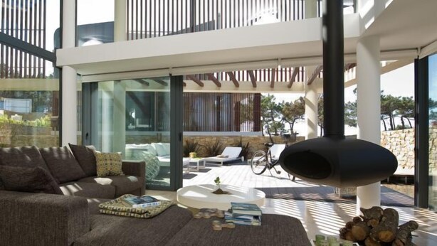 A modern living room with a large sectional sofa, a coffee table, and a fireplace. There is a balcony with a railing and a view of the outdoors. - Areias do Seixo Charm Hotel & Residences (Torres Vedras)