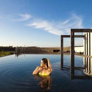 A person in a clear pool with a wooden structure on the right.