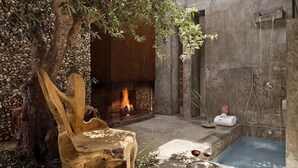 A stone-walled room with a fireplace, a wooden chair, a small pool, and a shower area. - Areias do Seixo Charm Hotel & Residences (Torres Vedras)