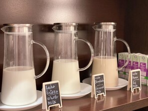 Three glass milk dispensers on a shelf with labels indicating different types of milk.