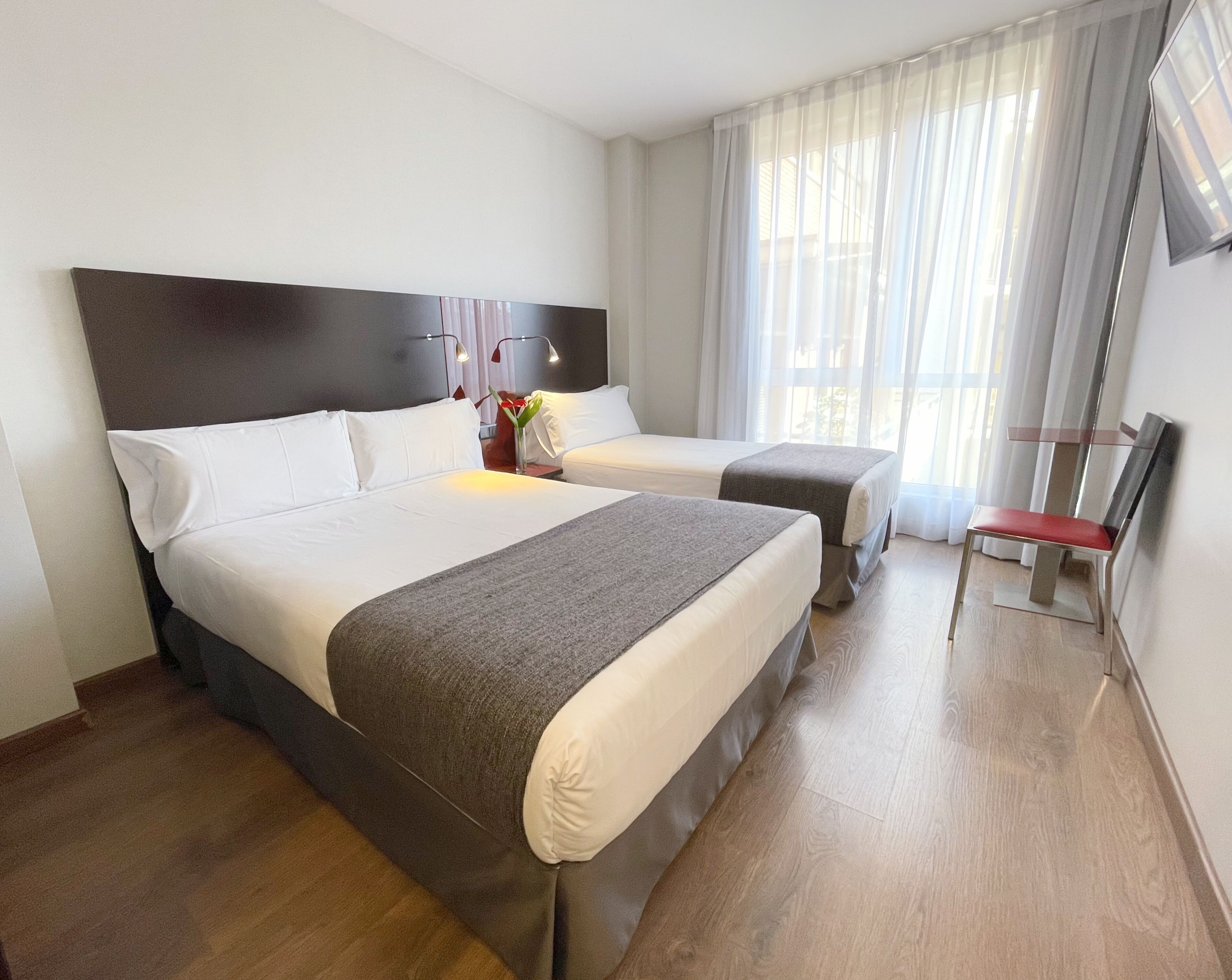 A hotel room with two beds, a TV, and a window with curtains.