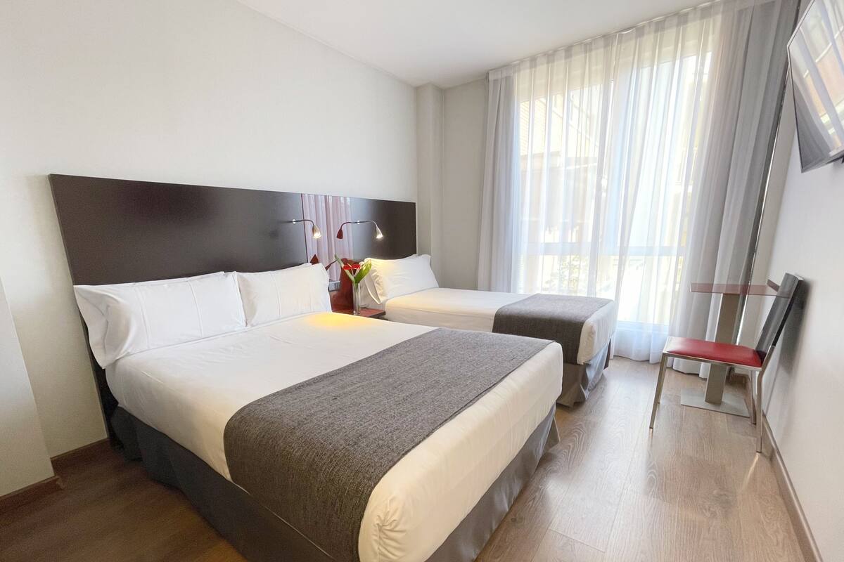 Ein Hotelzimmer mit zwei Betten, einem Fernseher und einem Fenster mit Vorhängen.
