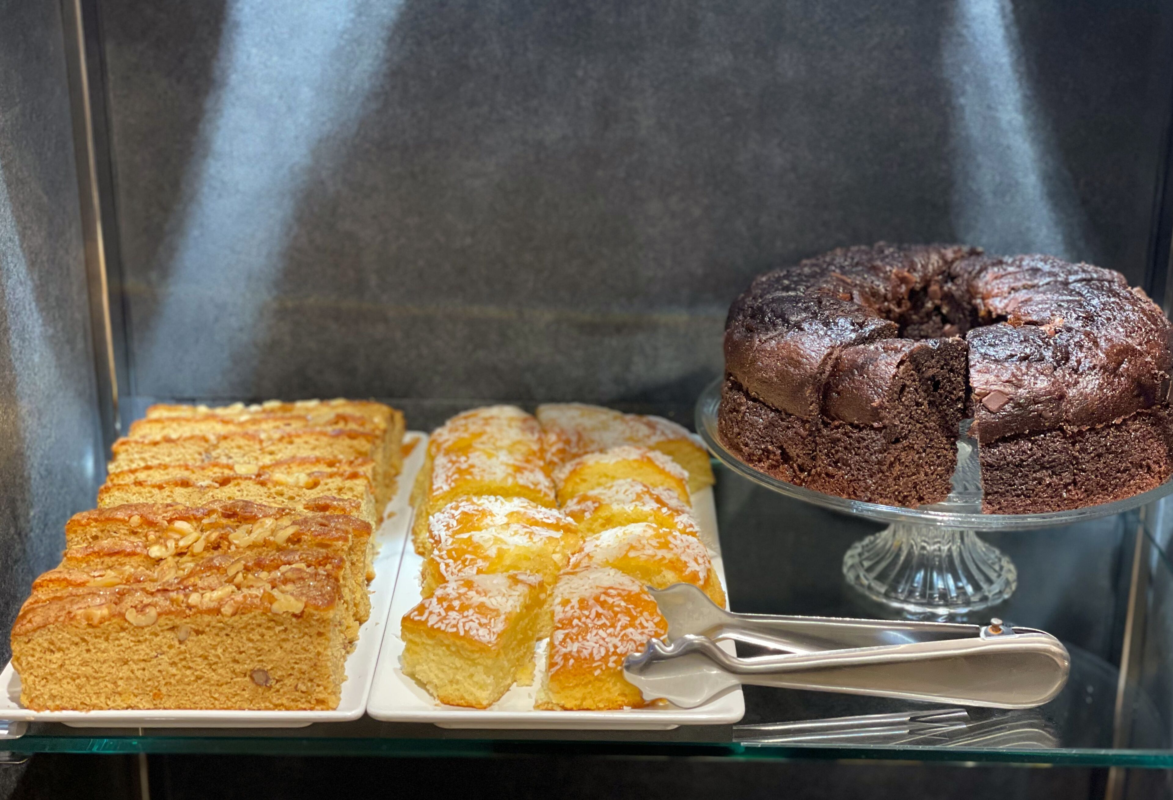 A display case with a variety of baked goods, including a chocolate cake and several types of bread.