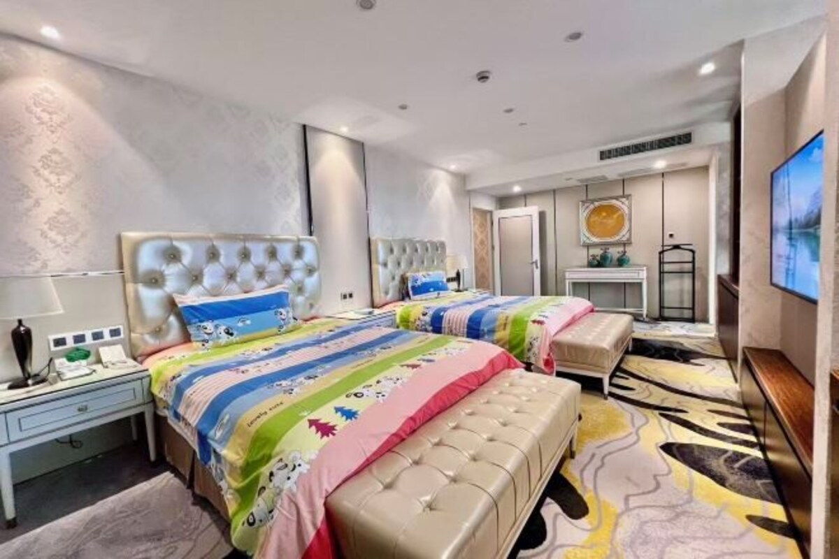 Una habitación de hotel moderna con dos camas, un espejo grande, un televisor y un baño con espejo y lavamanos.