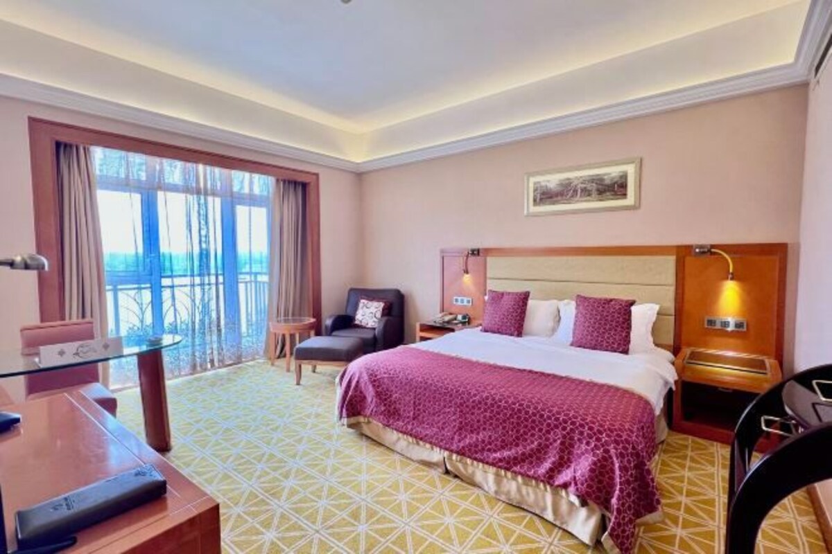 Habitación de hotel con una cama grande, un escritorio, una silla, un balcón y vistas al exterior.