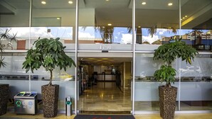 A hotel entrance with a reception desk, two large potted plants, a recycling bin, and a doormat with the hotel's name. - Best Western Plus Hotel San Diego (Medellín)