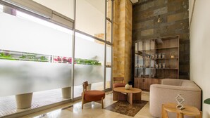 A modern interior with a large glass wall, a stone accent wall, a round wooden table, and a cushioned seating area. - Best Western Plus Hotel San Diego (Medellín)