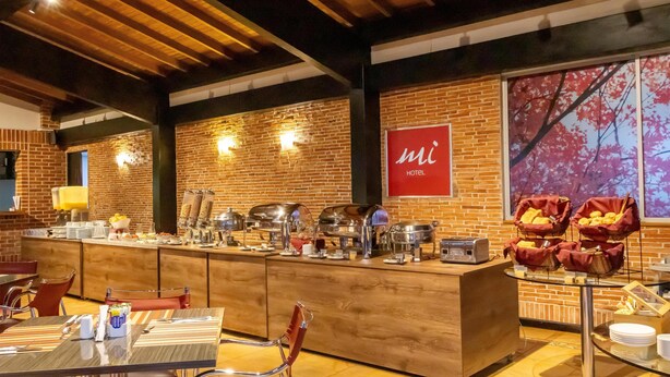 A hotel breakfast area with a buffet, seating, and a brick wall. - Best Western Plus Hotel San Diego (Medellín)
