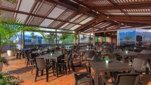 An outdoor dining area with tables and chairs, large windows, and a view of the city. - Best Western Plus Hotel San Diego (Medellín)