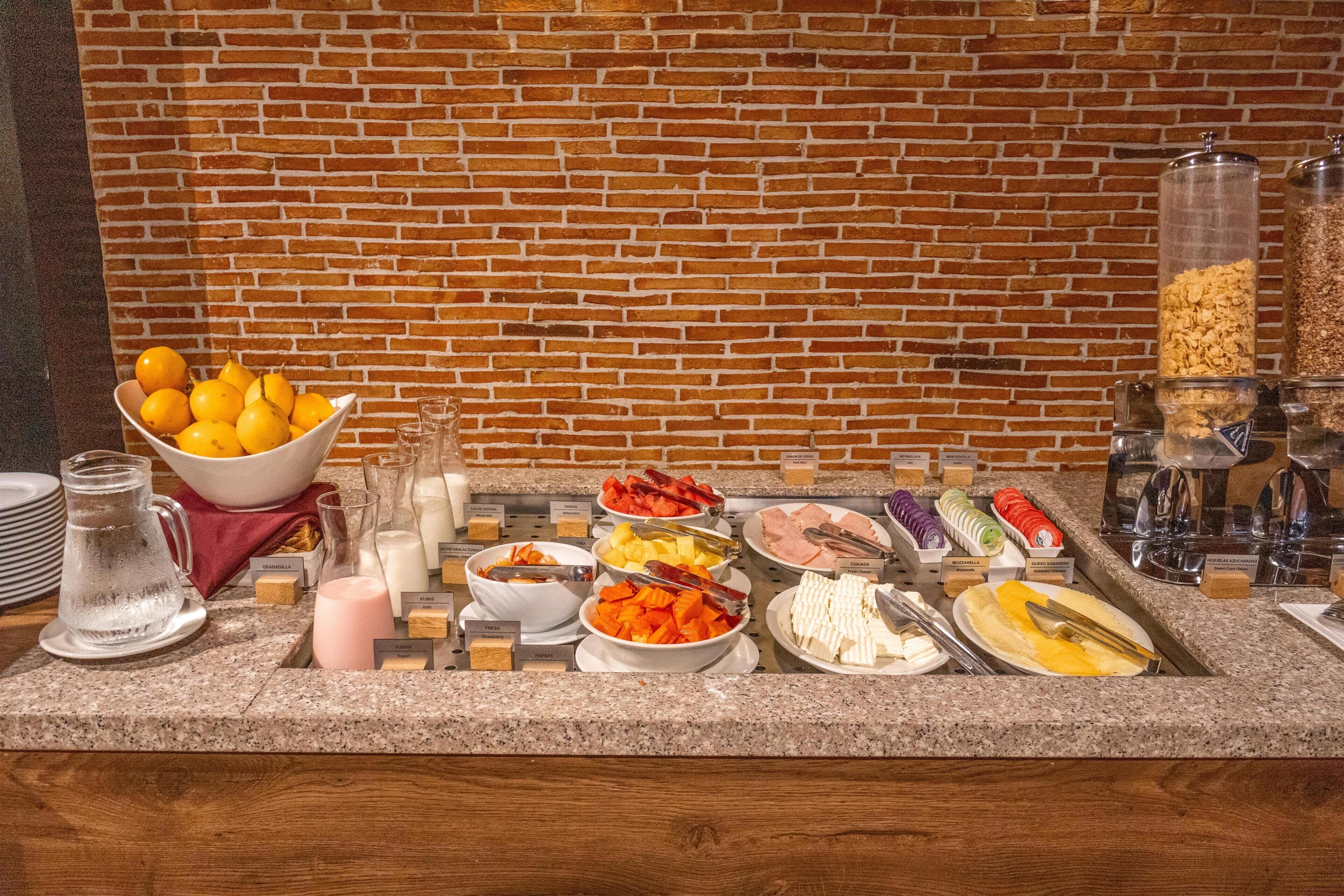 A breakfast buffet with various food items and condiments, set against a brick wall.