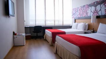 A hotel room with two beds, a desk, a refrigerator, and a television.