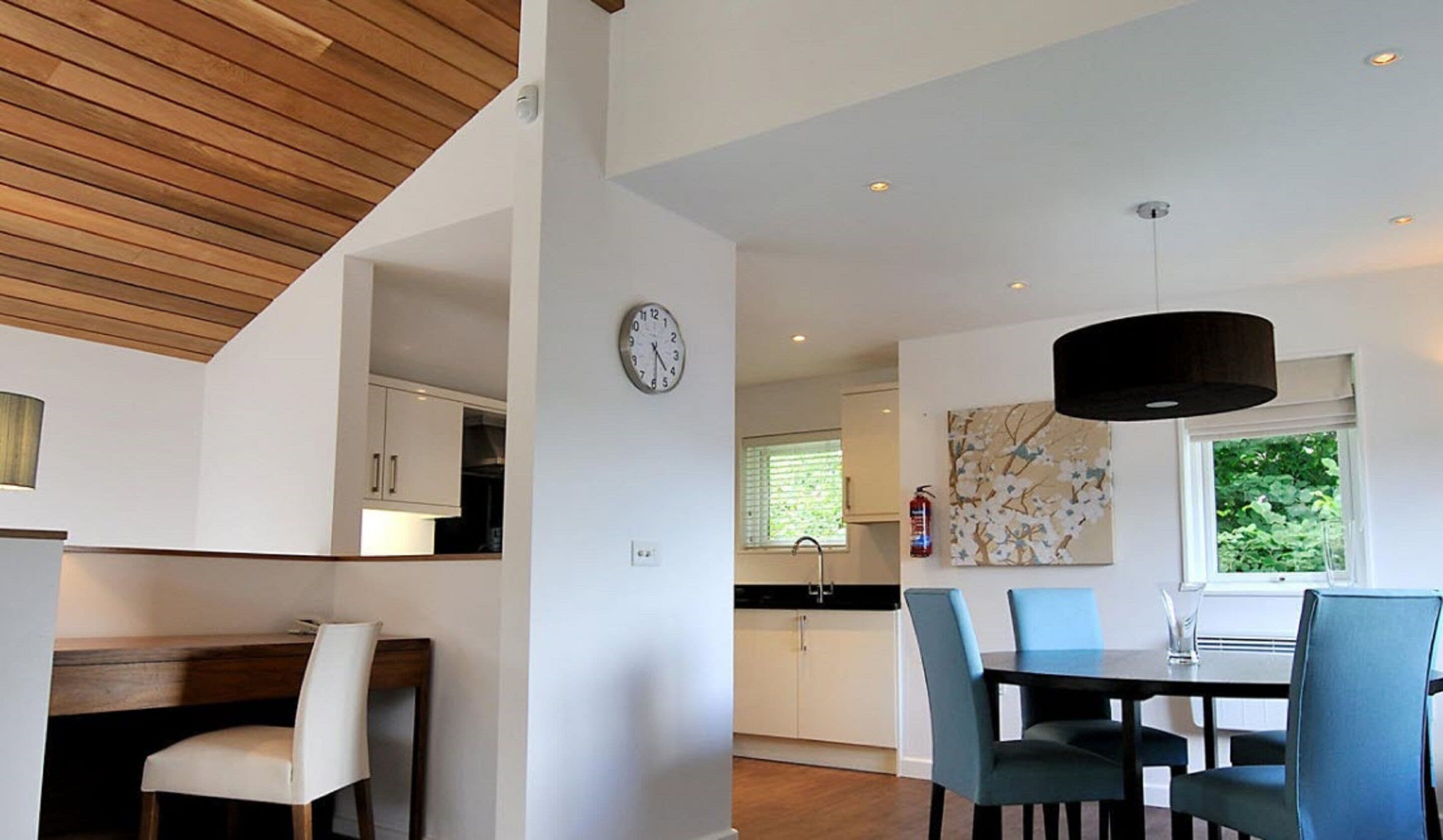 A modern kitchen with white cabinets, a clock, and a dining area with blue chairs and a wooden table.