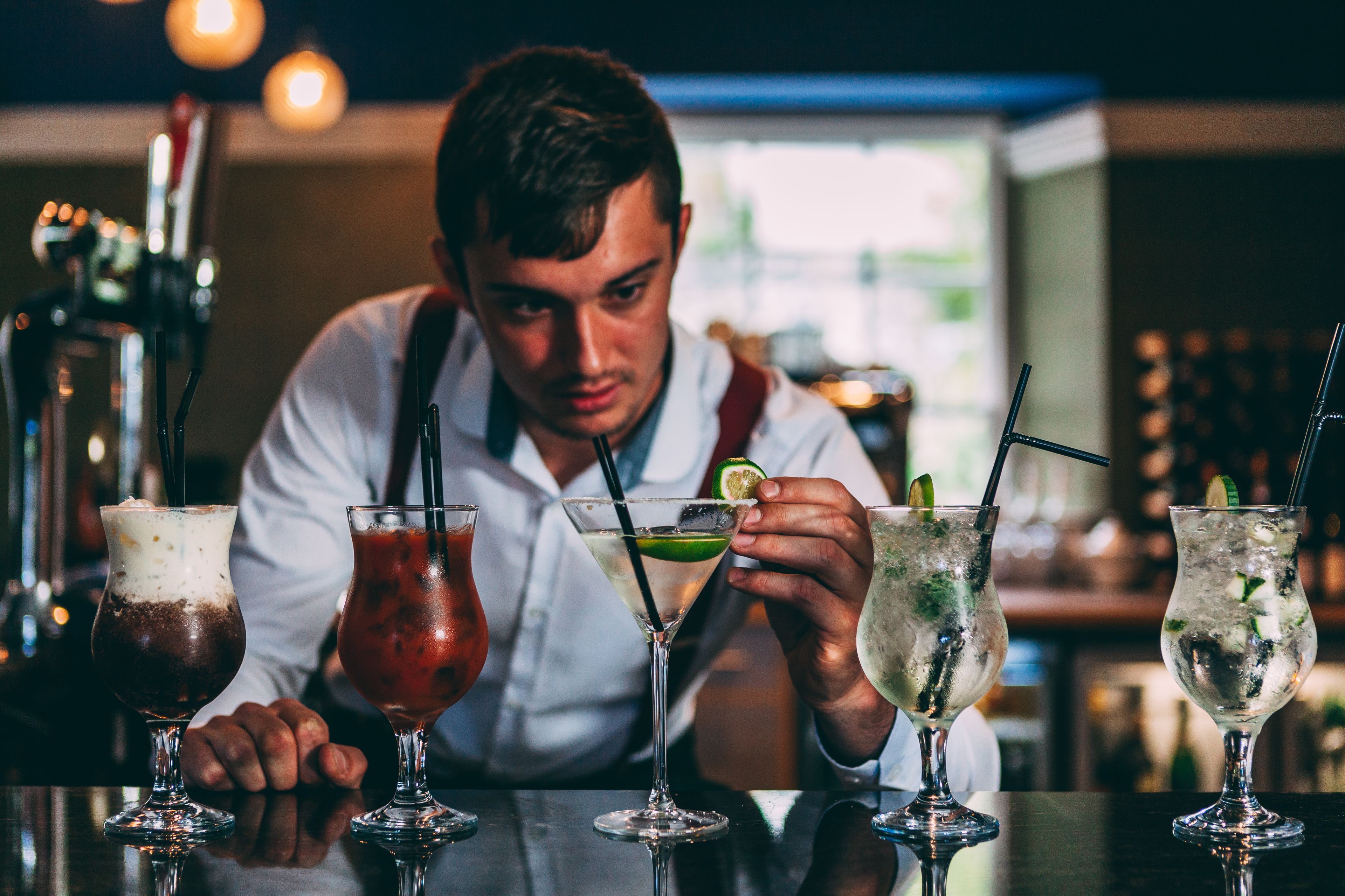 A bartender preparing drinks at a bar with various cocktail glasses on the counter.