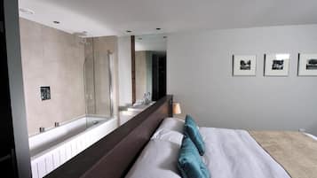 Habitación de hotel moderna con una cama grande, ducha integrada, espejo amplio y lavamanos empotrado en la pared.