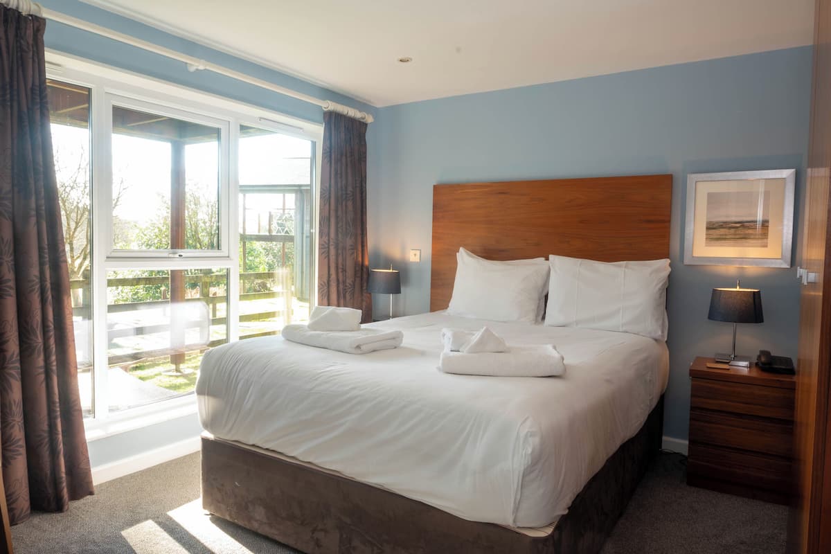 A neatly made bed with white linens and towels, a wooden headboard, and a bedside table with a lamp.