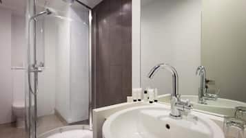 A modern bathroom with a glass-enclosed shower, a large sink with a mirror, and toiletries on the counter.