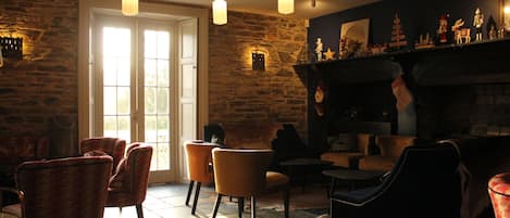 A cozy room with stone walls, a fireplace, and several chairs.