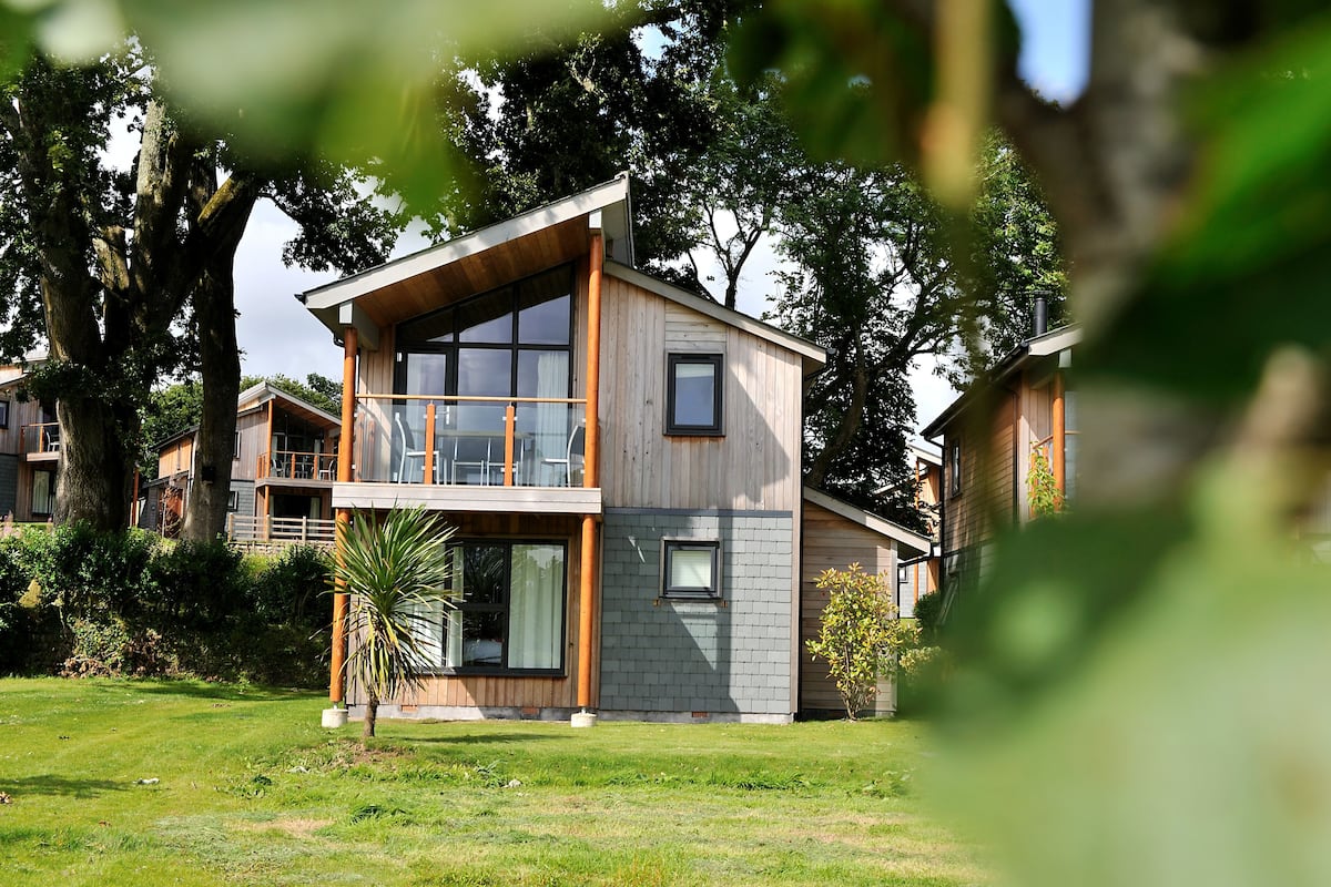 A modern two-story house with a balcony, large windows, and a well-maintained lawn.