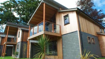 A modern two-story house with a balcony, large windows, and a well-maintained lawn.