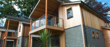 Una casa moderna de dos pisos con balcón, ventanas grandes y césped cuidado.