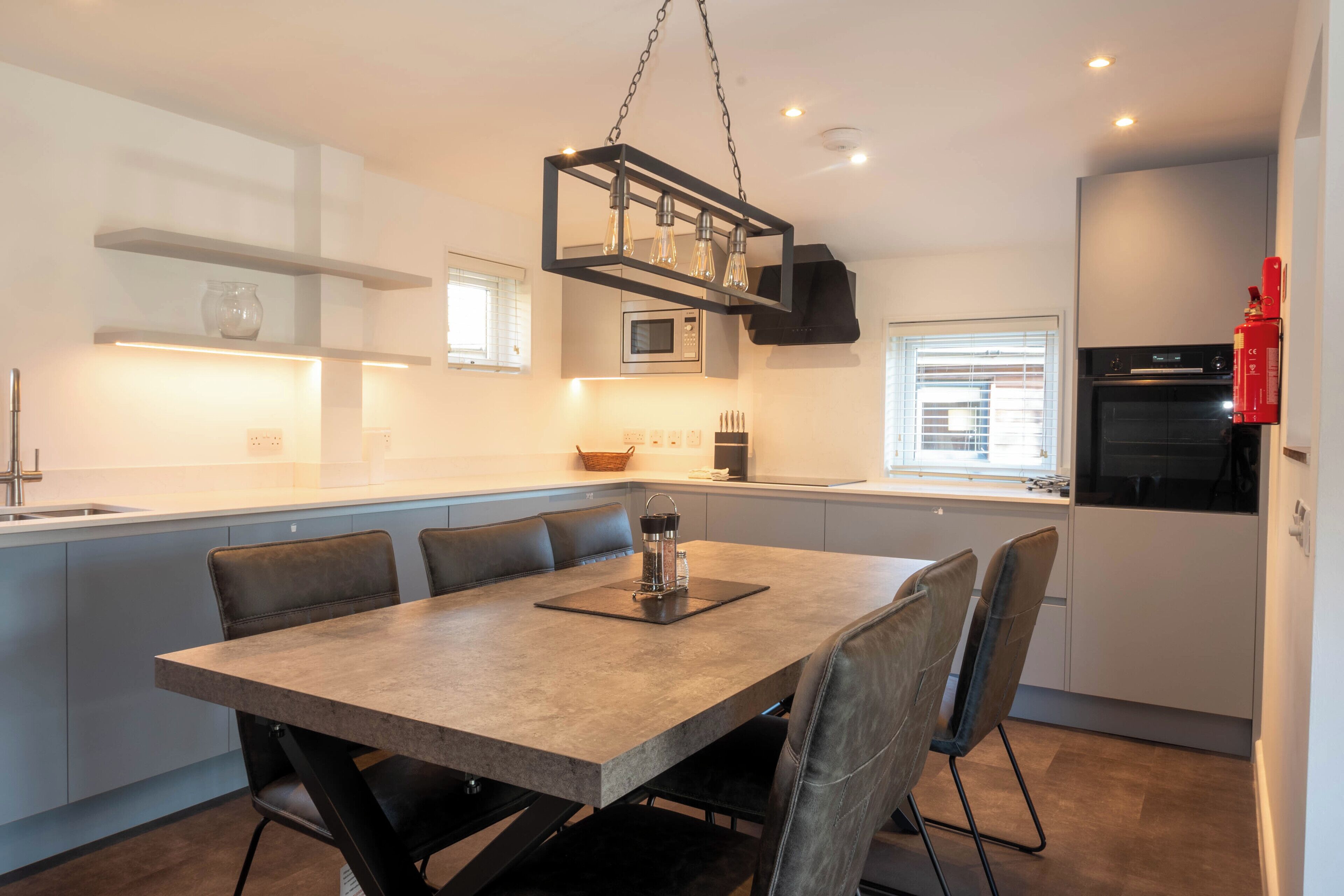 A modern kitchen with a dining area, featuring a central island, built-in appliances, and a pendant light.