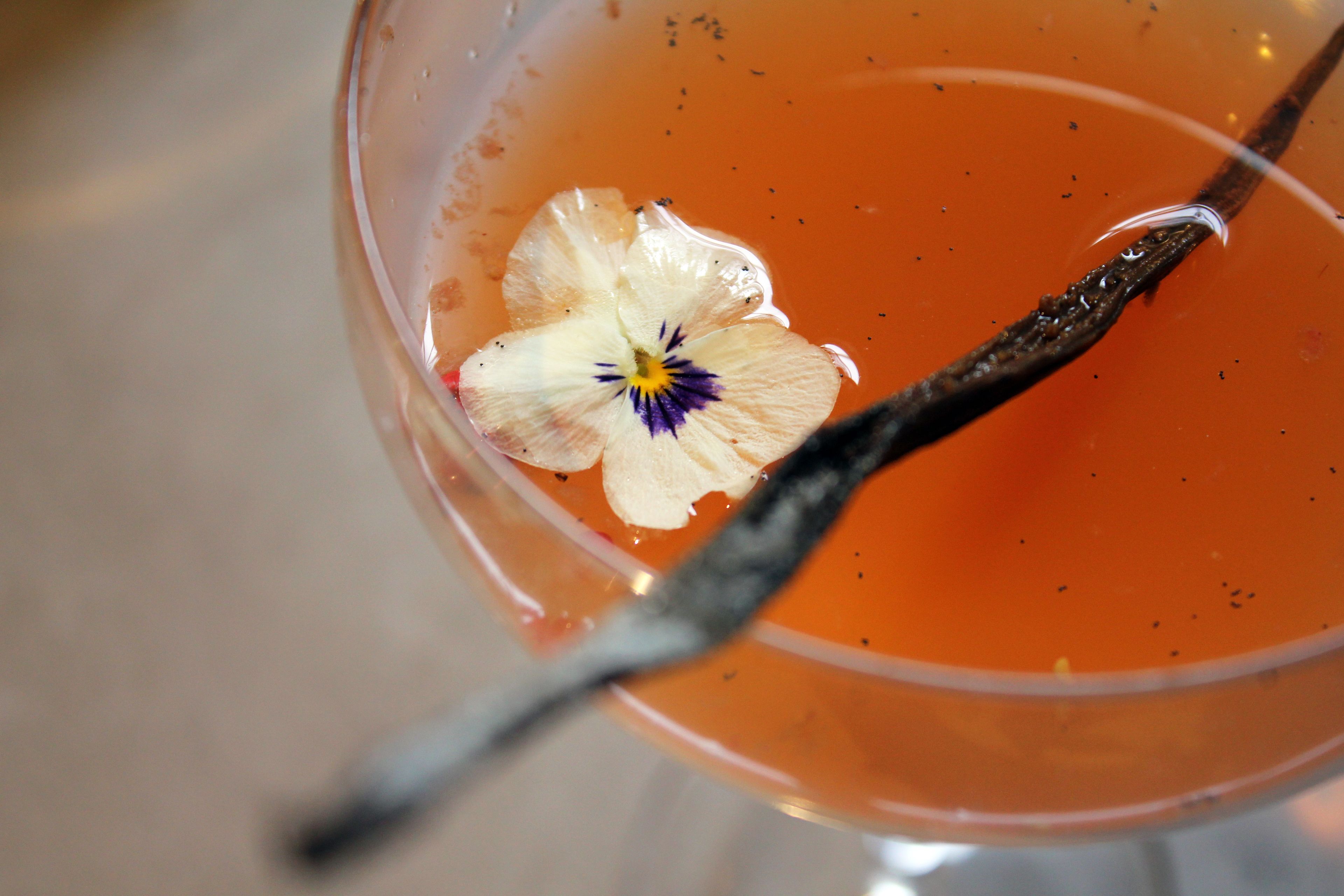 A close-up of a cocktail with a flower and a cinnamon stick.