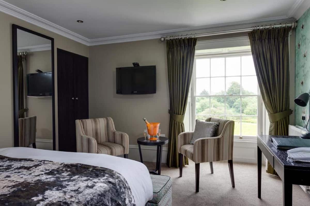 A hotel room with a bed, two armchairs, a desk, a television, and a window with curtains.