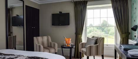 A hotel room with a bed, two armchairs, a desk, a television, and a window with curtains.