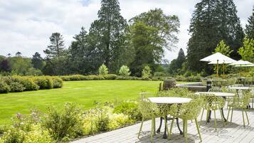 A patio area with tables and chairs, surrounded by a well-maintained lawn and tall trees.
