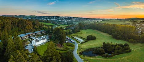An aerial view of a rural area with a large building, possibly a hotel, surrounded by green fields and trees.